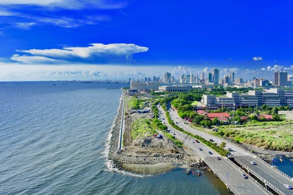 Aerial view of Manila Bay, Philippines, with a stunning cityscape, coastal roads, and the blue sea under a bright sky.