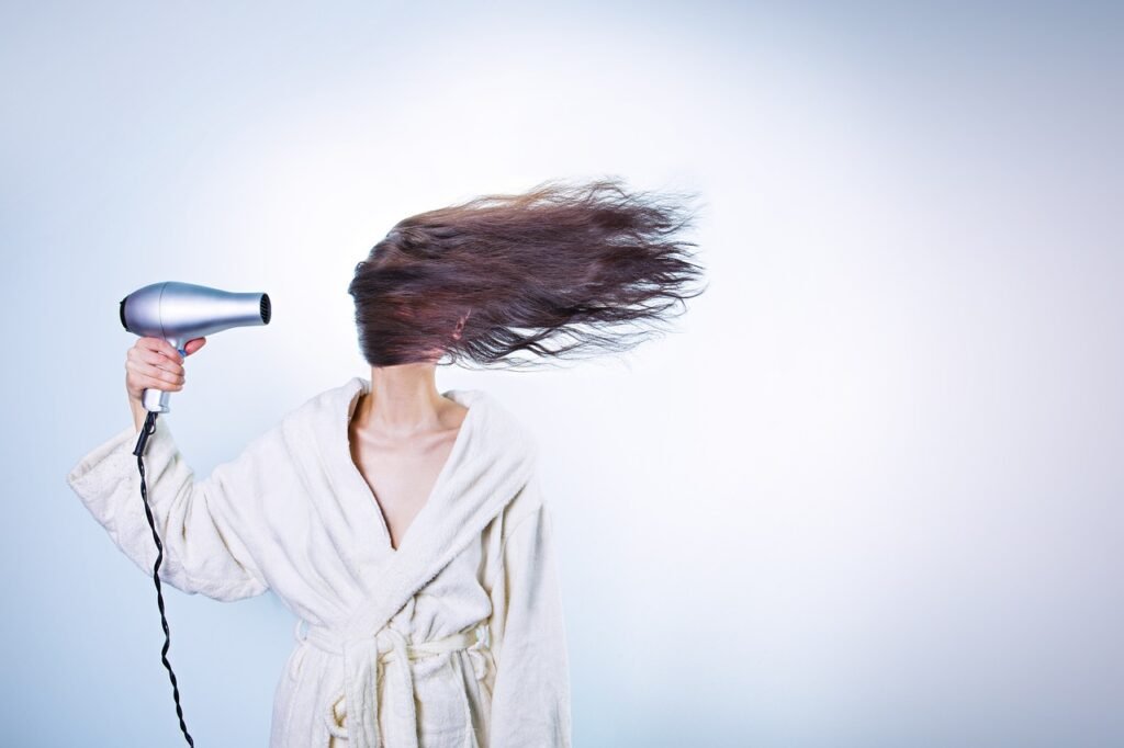 A woman in a bathrobe using a hair dryer, blowing her hair back.
